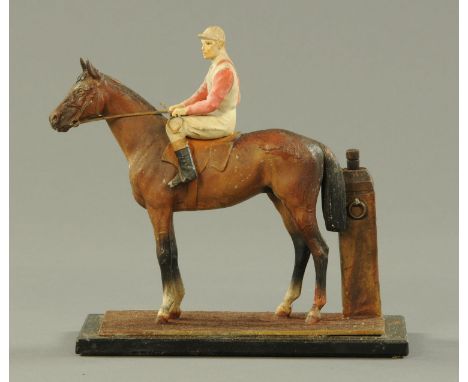 A spelter painted horse and jockey table lighter, raised on a rectangular glass base.  Length 17.5 cm. 