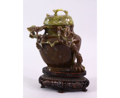 A CHINESE CARVED JADE VASE &amp; COVER, carved with foliage, fitted upon a carved wooden base, 17cm high, (AF)