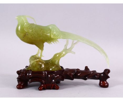 A CHINESE CARVED JADE MODEL OF A PEACOCK, stood upon stylized wooden outcrop,  on a carved hardwood base, 15cm high x 20cm wi