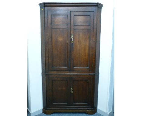 A GEORGE III OAK FLOORSTANDING CORNER CUPBOARD having double panel twin upper doors and original green paint interior, over s