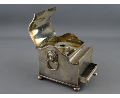 AN ELECTROPLATED SINGLE BOTTLE DESK STAND of casket form with shaped lid and pen aperture, lion mask ring handles and lower f