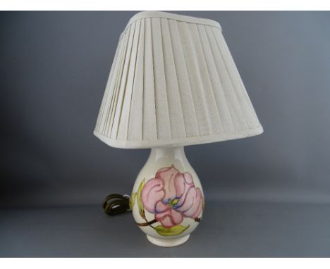 A MOORCROFT 'MAGNOLIA' TABLE LAMP decorated on a cream ground, impressed factory marks, with pleated shade, 37 cms high overa