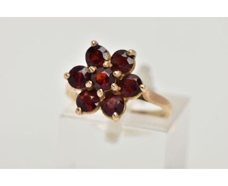 A YELLOW METAL GARNET CLUSTER RING, in the form of a flower cluster, set with seven circular cut garnets, raised openwork gal