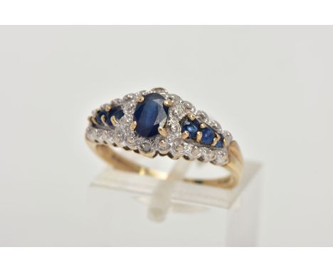 A 9CT GOLD SAPPHIRE RING, designed with a central four claw set, oval cut blue sapphire, flanked with six circular cut blue s