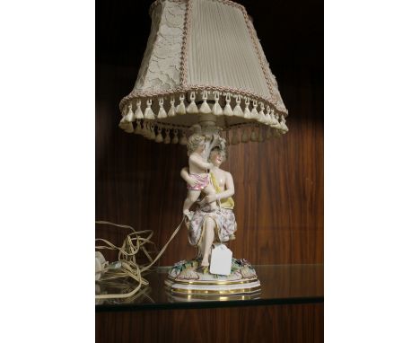 A CONTINENTAL PORCELAIN FIGURATIVE TABLE LAMP, modelled as a lady holding a child on a gilt lined and floral encrusted base, 