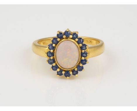 OPAL RING GG 750. Ringmaß 59.5. Ges.-Gew.: 5,29 g. Ein ovaler Opal Cabochon ca. 9,07 x 7,27 mm; 16 rund facettierte Saphire, 