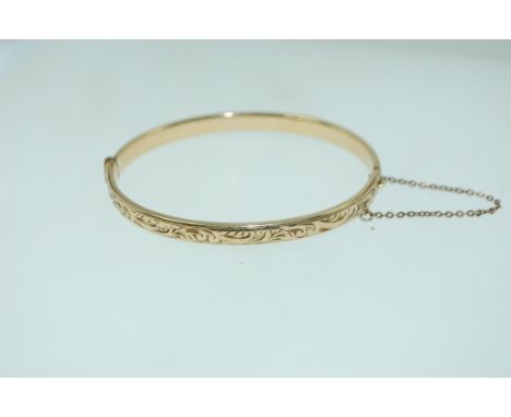 A yellow metal rolled gold bracelet bangle with foliate engraving, invisible clip clasp and safety chain. Marked Metal core W