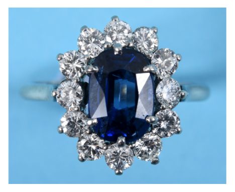 An 18ct white gold ring, the central sapphire within a surround of twelve diamonds, approx. ring size N See colour illustrati