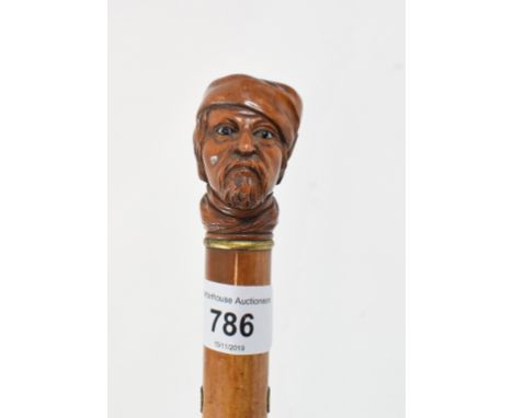 A walking stick, the wooden handle carved with a man wearing a hat 