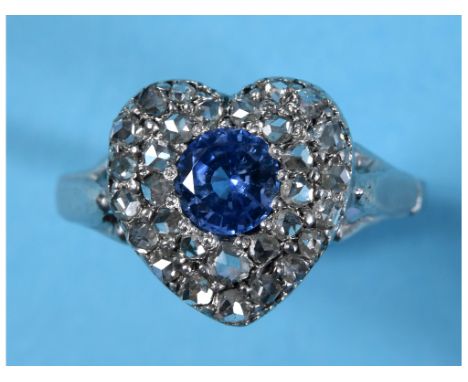 A white coloured metal and heart shaped ring, having a central sapphire within a surround of diamonds, approx. ring size N, a