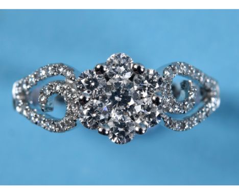 An 18ct white gold ring, the central flowerhead cluster of seven diamonds within a pierced scroll setting, approx. ring size 