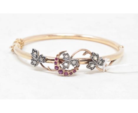 A gold bangle, set diamonds and garnets in the form of scrolling foliage, apparently unmarked 