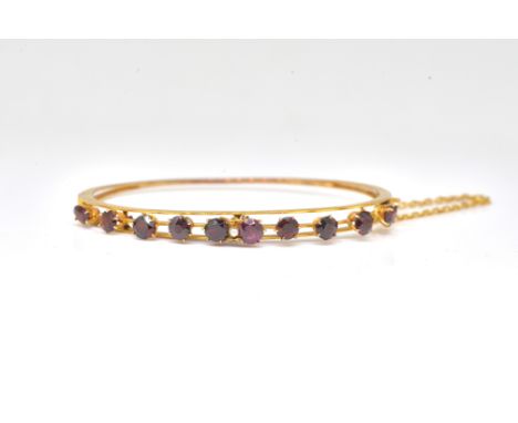A GOLD AND GARNET OVAL HINGED BANGLEThe front claw set with a row of circular cut garnets and with a central seed pearl, deta