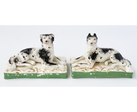 AN UNUSUAL PAIR OF STAFFORDSHIRE PORCELAIN WORKING DOGS (2)Circa 1840Each recumbent black and white hound modelled with an al