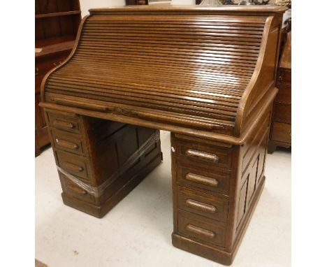 An early 20th Century oak tambour top desk, the lock plate inscribed "The Lebus desk" raised on two banks of four drawers to 