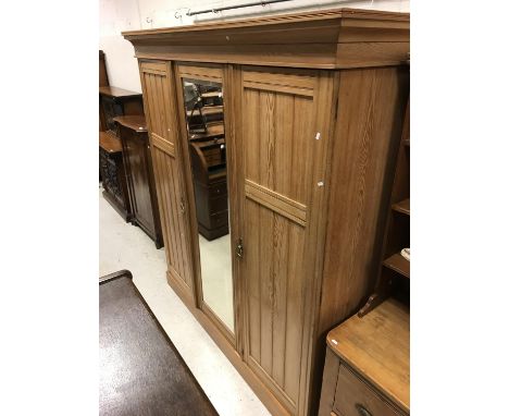 A Victorian ash triple wardrobe with central mirrored door enclosing a linen shelf (two missing) over three drawers flanked b