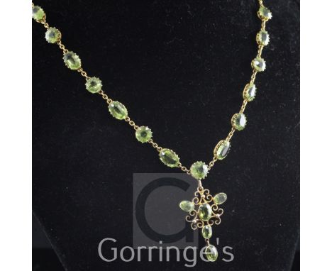 An Edwardian 9ct gold and peridot pendant necklace, set with twenty six round or oval cut stones, pendant 1.5in, chain 16in.