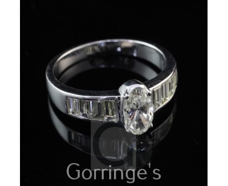 A 14ct white gold and diamond dress ring, set with central oval cut diamond and graduated baguette cut diamond set shoulders,