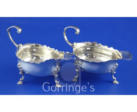 A pair of late George II silver sauce/cream boats, with flying scroll handles and shaped cut rims, on tripod hoof feet, Rober