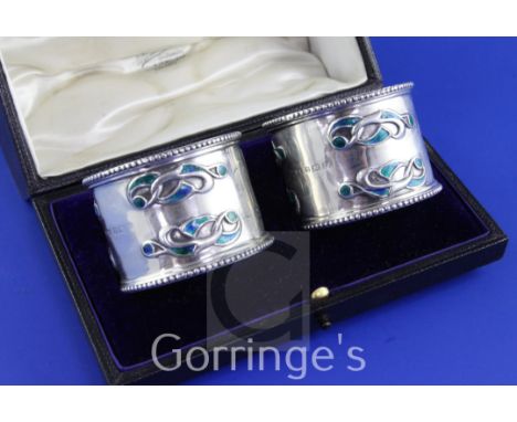 A cased pair of Edwardian Art Nouveau silver and enamel napkin rings by William Hair Haseler, with enamelled stylised scroll 