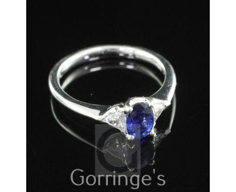 A modern 18ct white gold, sapphire and diamond ring, with central oval cut blue sapphire flanked by trilliant cut diamonds, s