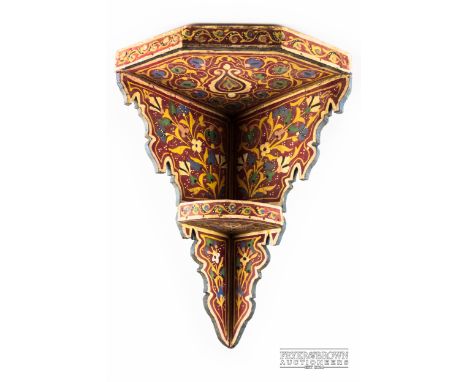 A Persian polychrome painted corner wall shelf, red ground with foliate motifs, 43cms