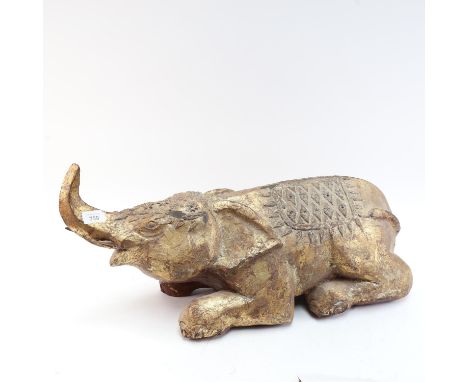 A large and heavy lacquered and gilded hardwood recumbent caparisoned elephant sculpture/foot rest, length 65cm, height 30cm,