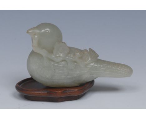 A Chinese pale green jade model, of a bird, holding a blossoming branch it its beak, 8cm long, hardwood stand