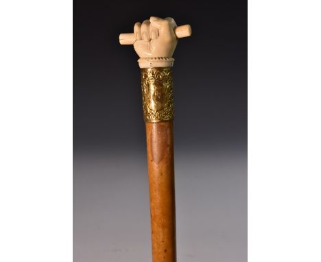 A 19th century ivory and malacca walking stick, the pommel boldly carved as a hand grasping a baton, yellow metal collar chas