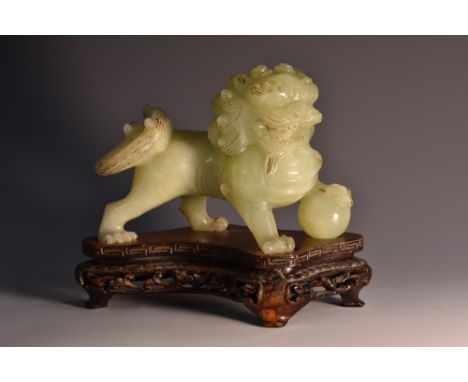 A Chinese celadon jade carving, of a Guardian Lion, his paw resting on a temari, menacing grin, fitted hardwood stand, 11cm h