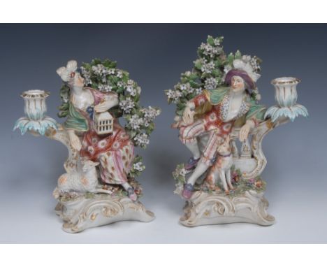 A pair of Derby Patch Mark figural candle sconce holders, modelled as a shepherd and shepherdess, each seated beneath a bower