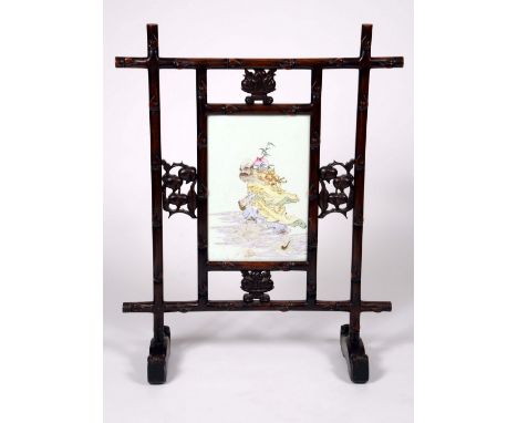 A Chinese porcelain mounted padouk wood fire screen, the rectangular panel painted in polychrome with a wise elder carrying a