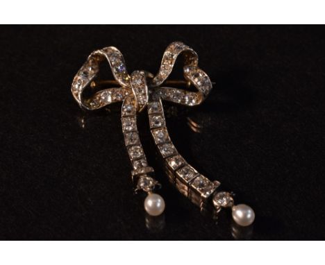 A diamond encrusted white metal ribbon bow brooch with pearl droplet terminals, encrusted with fifty four round and old cut d