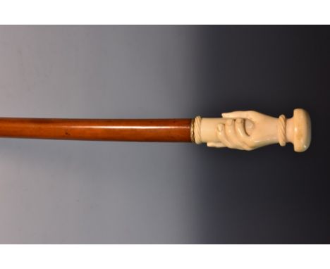 A 19th century novelty ivory and malacca walking stick, the pommel carved as a grasping hand, the shaft with yellow-metal fer