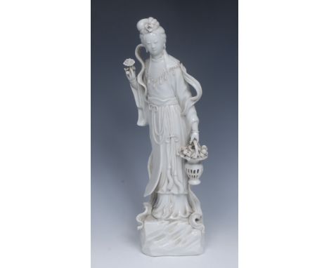 A Chinese Blanc de Chine figure, of Guanyin, holding a magnolia blossom and a reticulated basket of further blossoms, her dre