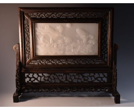 A Chinese white jade and hardwood table screen, the rectangular panel carved in high relief with a lakeside scenes of carp sp