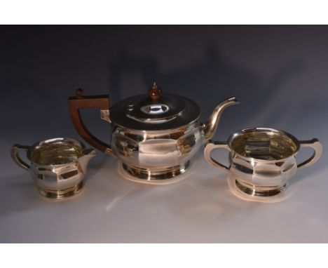 An Art Deco silver three piece panelled pedestal tea service, comprising teapot, milk jug and sugar basin, angular scroll han