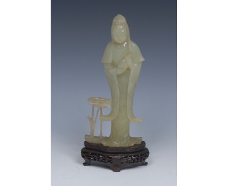 A Chinese jade carving, of Guanyin, standing in flowering robes by lotus, pierced hardwood stand, 22.5cm high