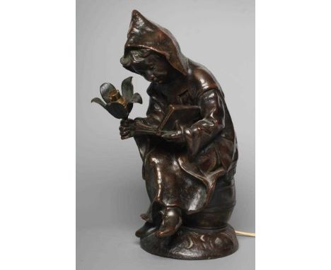 A BRONZED METAL FIGURAL TABLE LAMP, 20th century, modelled as a hooded child seated on a barrel, holding a light and reading 