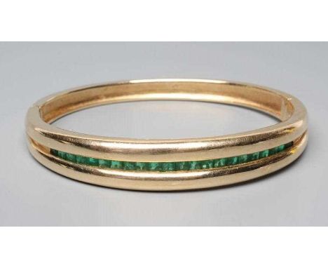 AN EMERALD STIFF HINGED BANGLE, the upper section channel set with twenty two graduated calibre square cut stones to a plain 