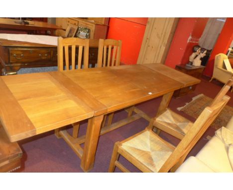 A contemporary light oak draw leaf dining table together with four matching chairs having rush seats