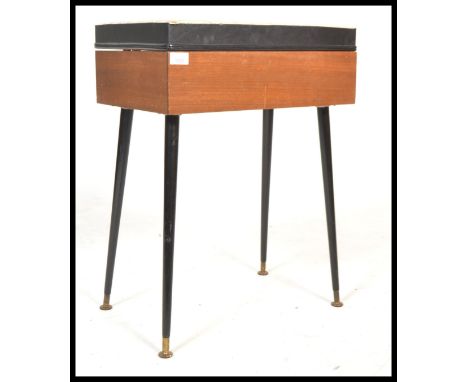 A vintage 20th century retro teak sewing box raised on tapering ebonised legs with brass circular feet. The hinged lid openin