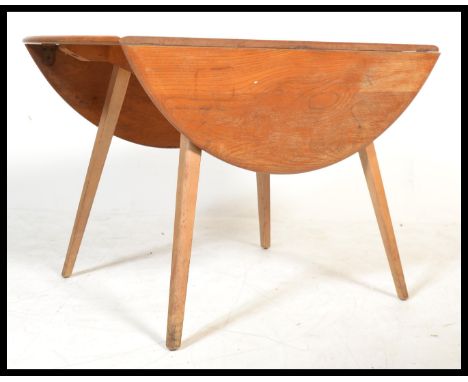 A retro mid 20th century beech and elm Ercol drop leaf circular dining table being raised on squared legs with drop leaves be