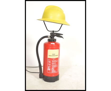 A 20th Century up-cycled fire extinguisher, converted in to a floor lamp surmounted with a firemans helmet&nbsp;