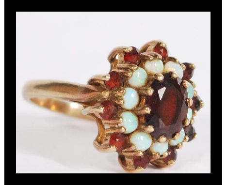 A hallmarked 9ct gold opal and garnet stone cluster ring having a central faceted red stone with a halo of opals and garnets.