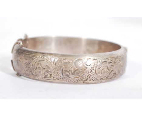A silver hallmarked rococo chase decorated bangle with clip clasp and safety chain. Hallmarked for Birmingham 1972, makers R.