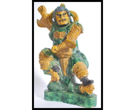 A large 19th century Chinese ceramic figure of a warrior with green and brown colouring. The man raised on a pedestal base wi