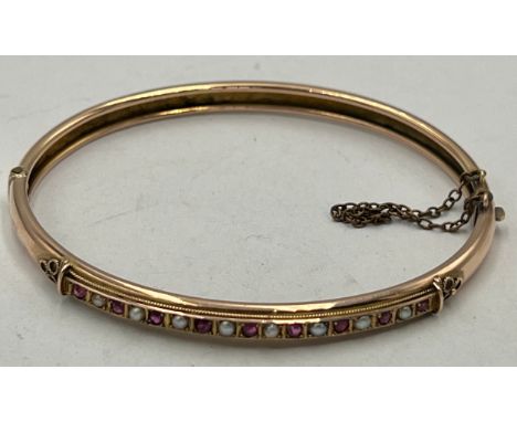 An unmarked yellow metal bangle set with rubies and seed pearls. Weight 6.2gm. Approximately 6cm x 5cm.