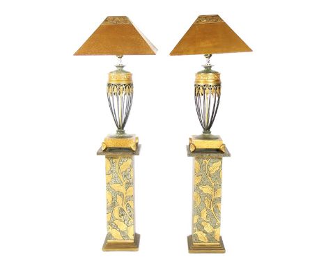 A pair of Art Deco style table lamps on painted wooden pedestals, the patinated metal lamps of pierced urn shape, the square 