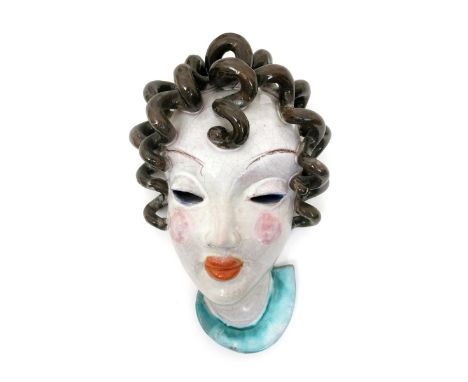 A Goldscheider Pottery wall mask, model no.1213, modelled as a stylised woman with brown curly hair, pierced elliptical eyes,